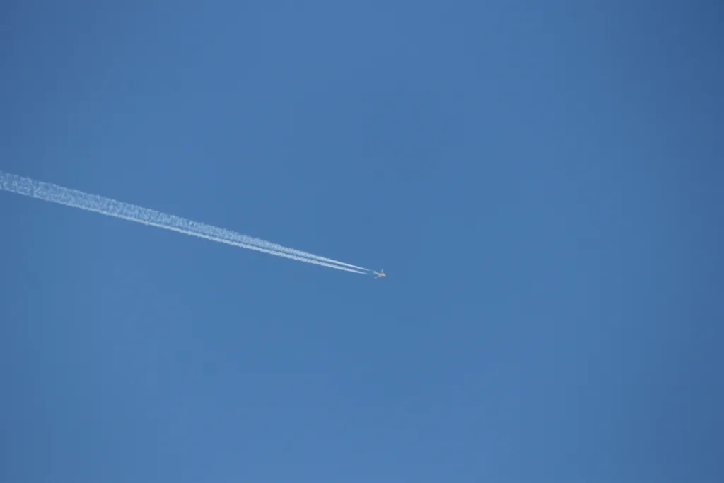 Airliner cruising in blue sky, leaving a white condensation trail