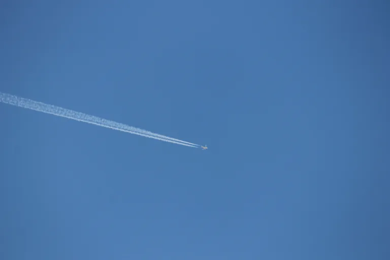 Airliner cruising in blue sky, leaving a white condensation trail