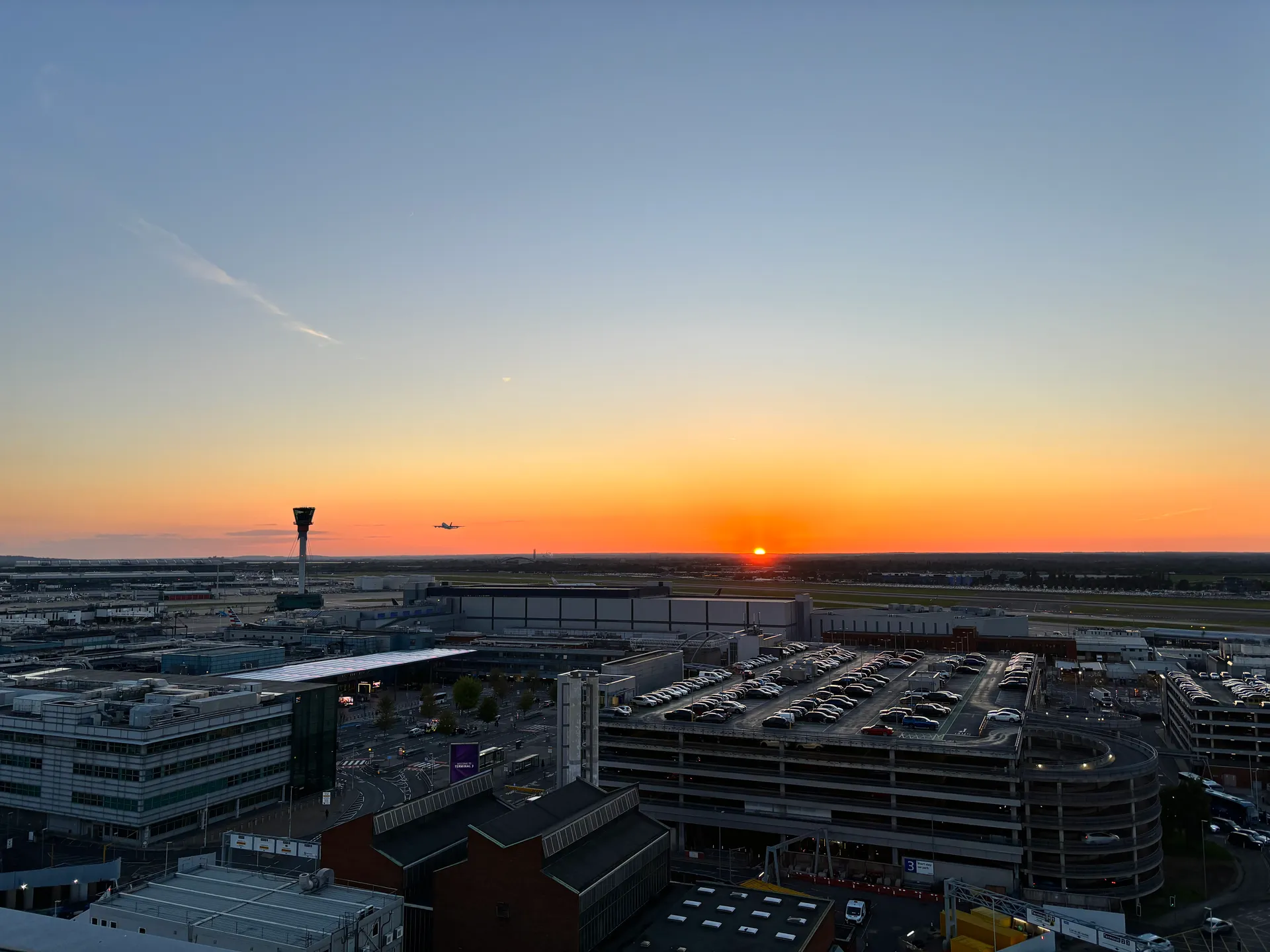 Aircraft approaching Heathrow Airport above a runway and control tower at sunset in June 2024